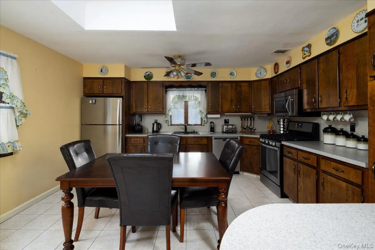 Kitchen featuring wood-finish cabinetry, stainless steel appliances, a white tile floor, and a skylight Kitchen featuring wood-finish cabinetry, stainless steel appliances, a white tile floor, and a skylight