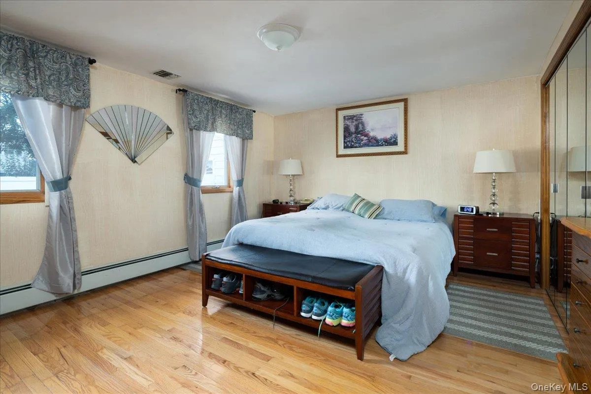 Warm wood-finish flooring with dual windows, built-in mirrored closet, and a ceiling-mounted light fixture Warm wood-finish flooring with dual windows, built-in mirrored closet, and a ceiling-mounted light fixture