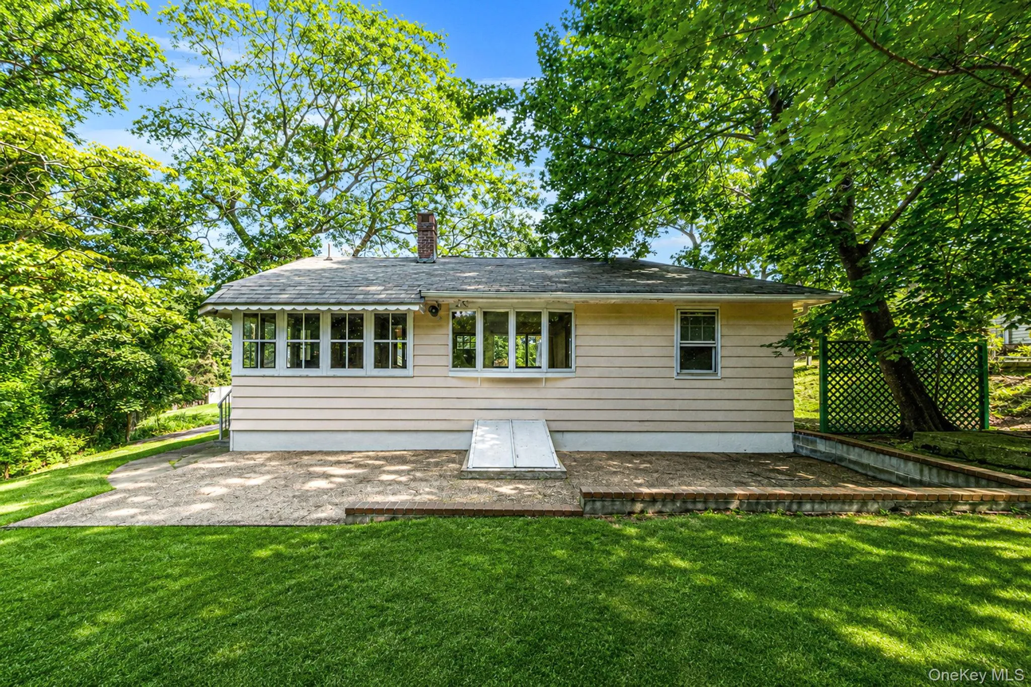 Expansive rear patio with retaining wall, mature trees, and well-maintained lawn Expansive rear patio with retaining wall, mature trees, and well-maintained lawn