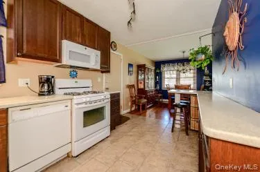Kitchen featuring wood cabinetry, light-toned countertops, tile flooring, and white appliances including a range and dishwasher Kitchen featuring wood cabinetry, light-toned countertops, tile flooring, and white appliances including a range and dishwasher