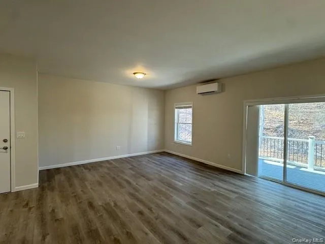 Empty room with dark wood-type flooring and an AC wall unit Empty room with dark wood-type flooring and an AC wall unit