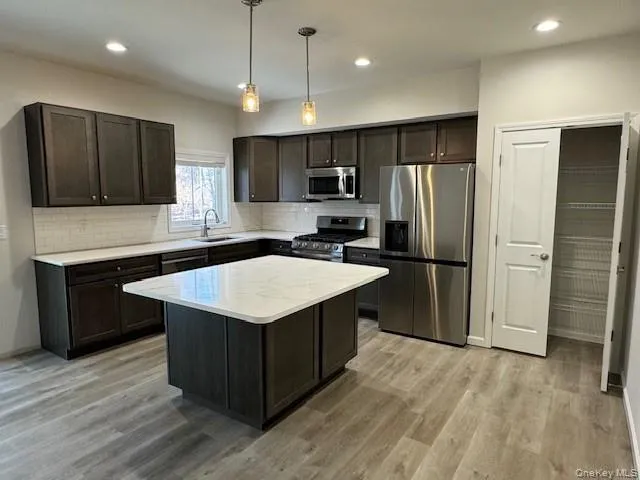 Kitchen featuring sink, a center island, light wood-type flooring, pendant lighting, and stainless steel appliances Kitchen featuring sink, a center island, light wood-type flooring, pendant lighting, and stainless steel appliances