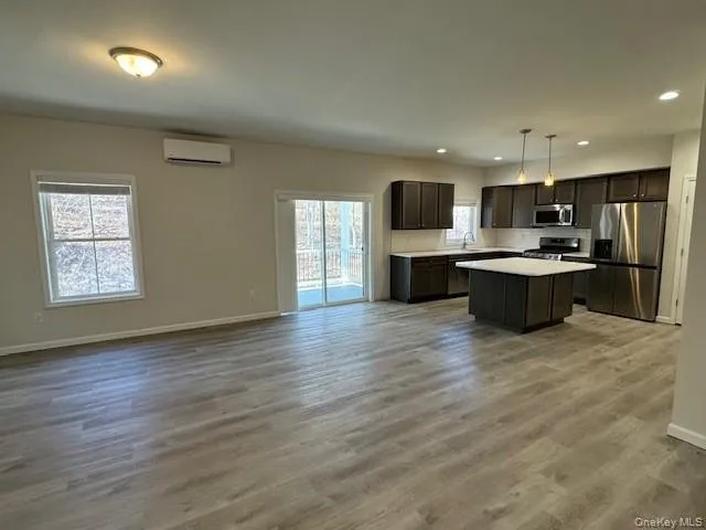 Kitchen featuring hanging light fixtures, plenty of natural light, stainless steel appliances, dark brown cabinetry, and an AC wall unit Kitchen featuring hanging light fixtures, plenty of natural light, stainless steel appliances, dark brown cabinetry, and an AC wall unit
