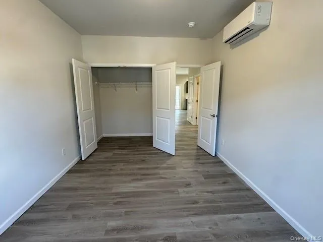 Unfurnished bedroom with dark wood-type flooring, a wall mounted AC, and a closet Unfurnished bedroom with dark wood-type flooring, a wall mounted AC, and a closet