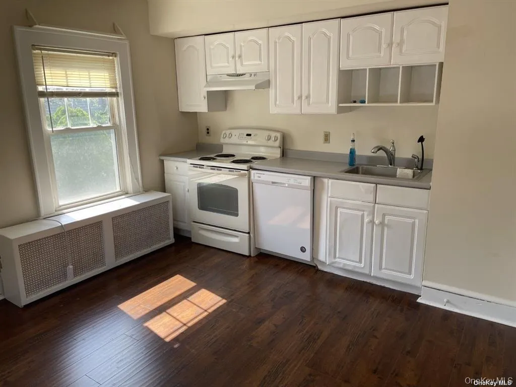 White cabinetry with an integrated range hood, a dishwasher, an electric range, and a stainless steel sink, complemented by wood-finish flooring White cabinetry with an integrated range hood, a dishwasher, an electric range, and a stainless steel sink, complemented by wood-finish flooring