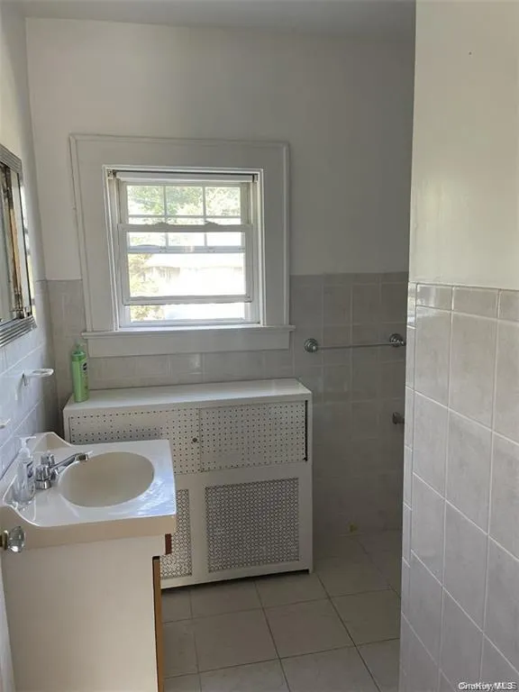 Window with white trim, white vanity with integrated sink, chrome faucet, tiled flooring, and tiled walls Window with white trim, white vanity with integrated sink, chrome faucet, tiled flooring, and tiled walls