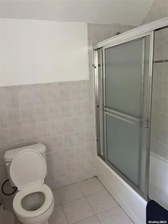 White tiled walls and flooring with a shower/tub combination featuring frosted sliding doors White tiled walls and flooring with a shower/tub combination featuring frosted sliding doors