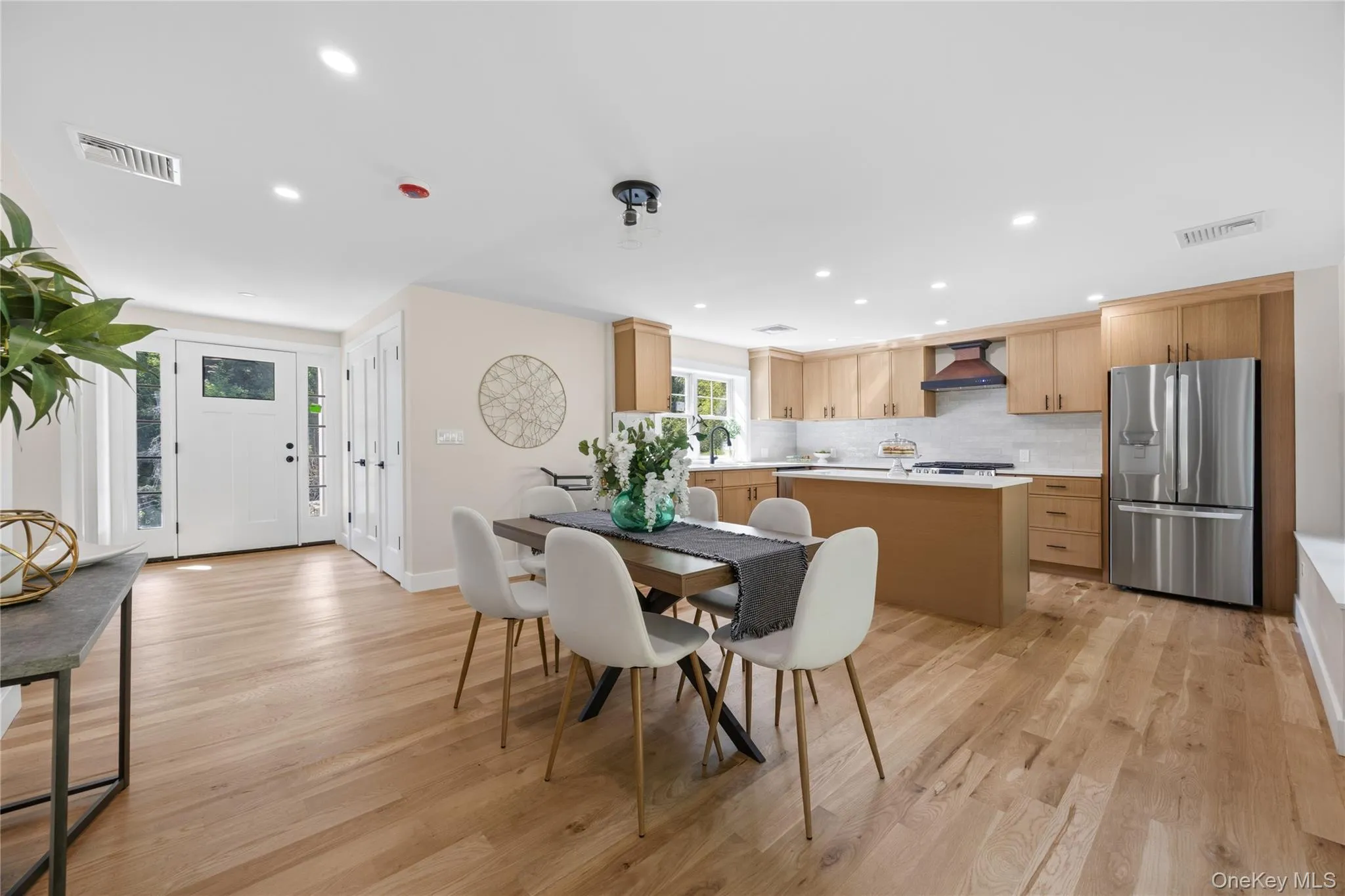 Light wood-finish flooring, recessed lighting, white perimeter walls, and a kitchen featuring wood cabinetry and an island Light wood-finish flooring, recessed lighting, white perimeter walls, and a kitchen featuring wood cabinetry and an island