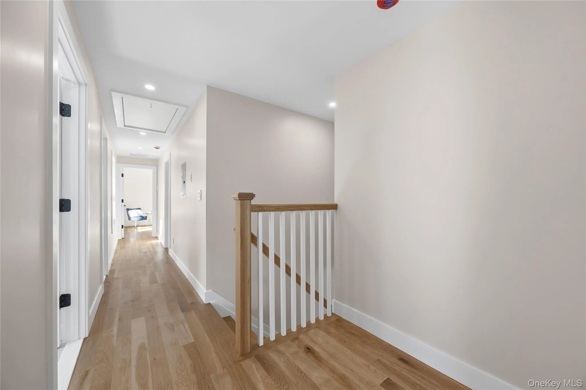Hallway with wood-finish flooring, white trim, recessed lighting, and a light wood and white spindle staircase railing Hallway with wood-finish flooring, white trim, recessed lighting, and a light wood and white spindle staircase railing