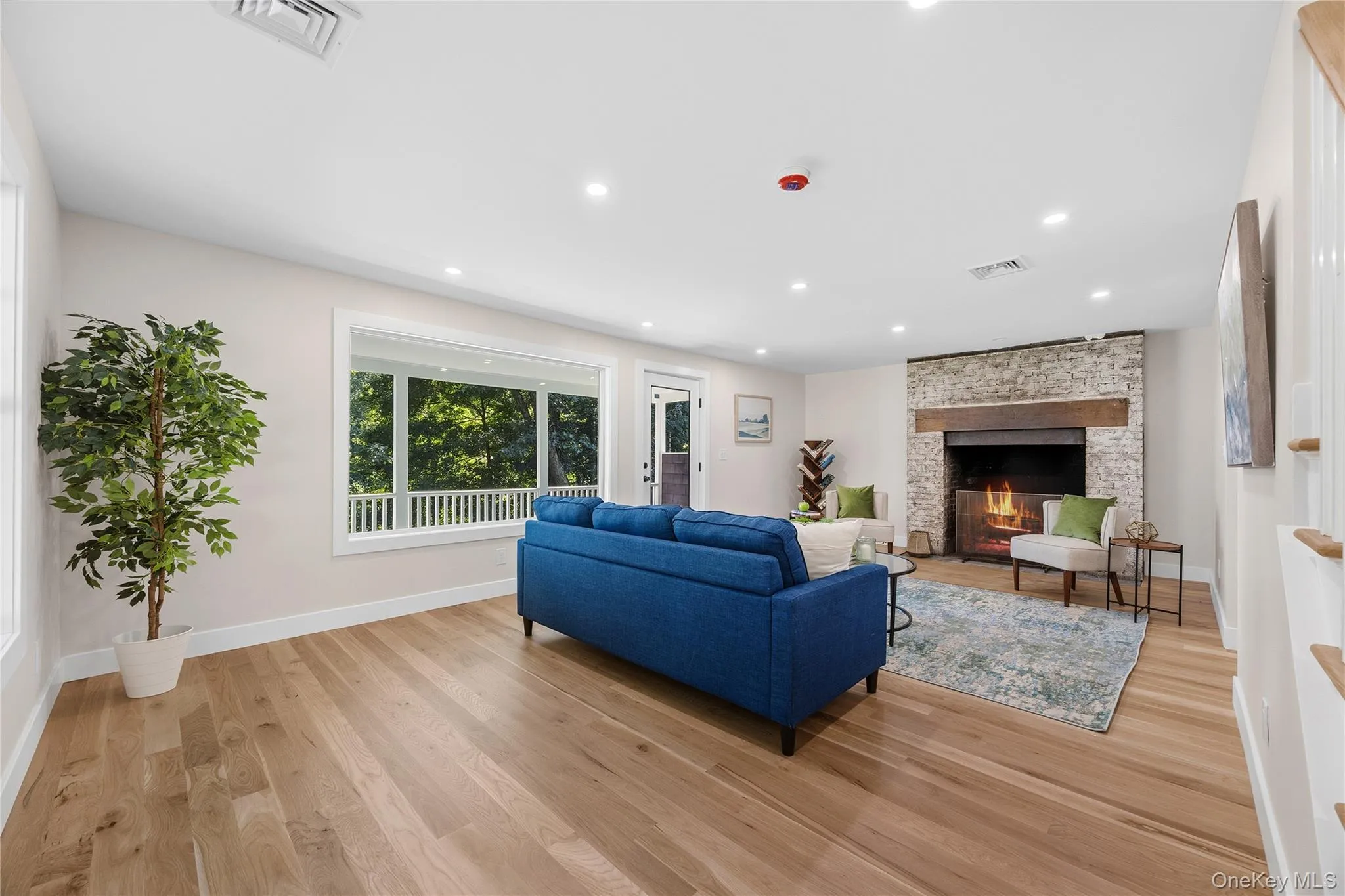 Hardwood flooring, recessed lighting, stone fireplace with wood mantle, white trim, and a covered porch Hardwood flooring, recessed lighting, stone fireplace with wood mantle, white trim, and a covered porch