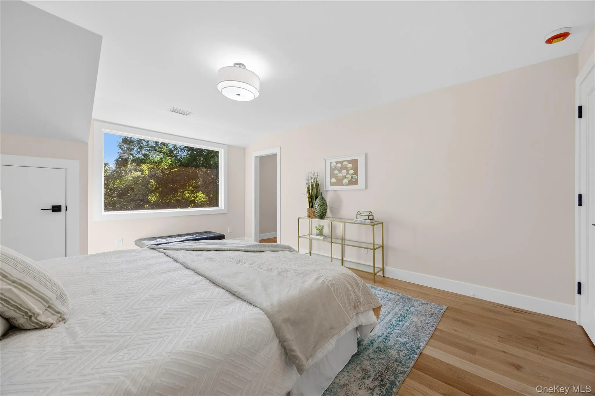 Hardwood flooring throughout, featuring a large picture window, modern flush-mount ceiling light, and crisp white trim Hardwood flooring throughout, featuring a large picture window, modern flush-mount ceiling light, and crisp white trim