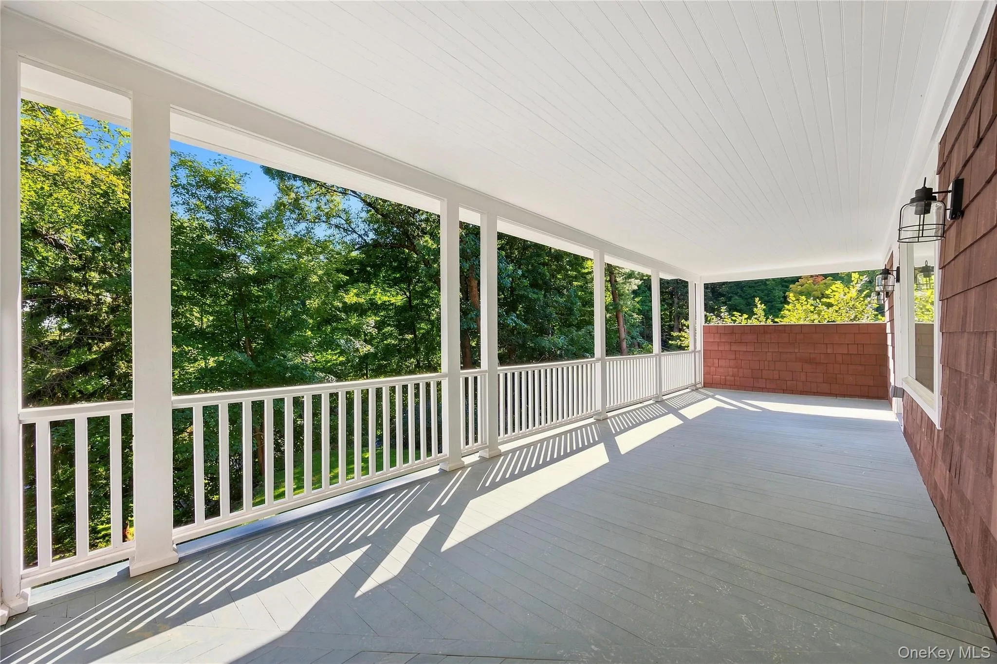 Spacious covered porch with perimeter railing, white columns, and wood-finish flooring Spacious covered porch with perimeter railing, white columns, and wood-finish flooring