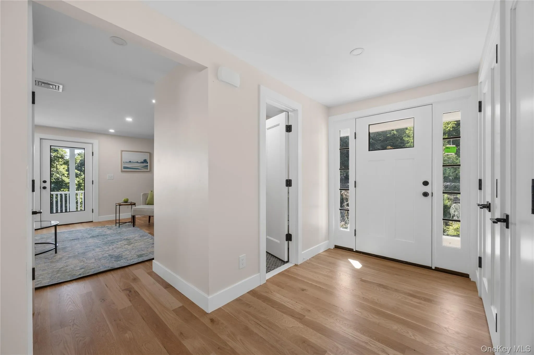 Wood-finish flooring throughout, white paneled doors, recessed lighting, and a white front door with sidelights Wood-finish flooring throughout, white paneled doors, recessed lighting, and a white front door with sidelights