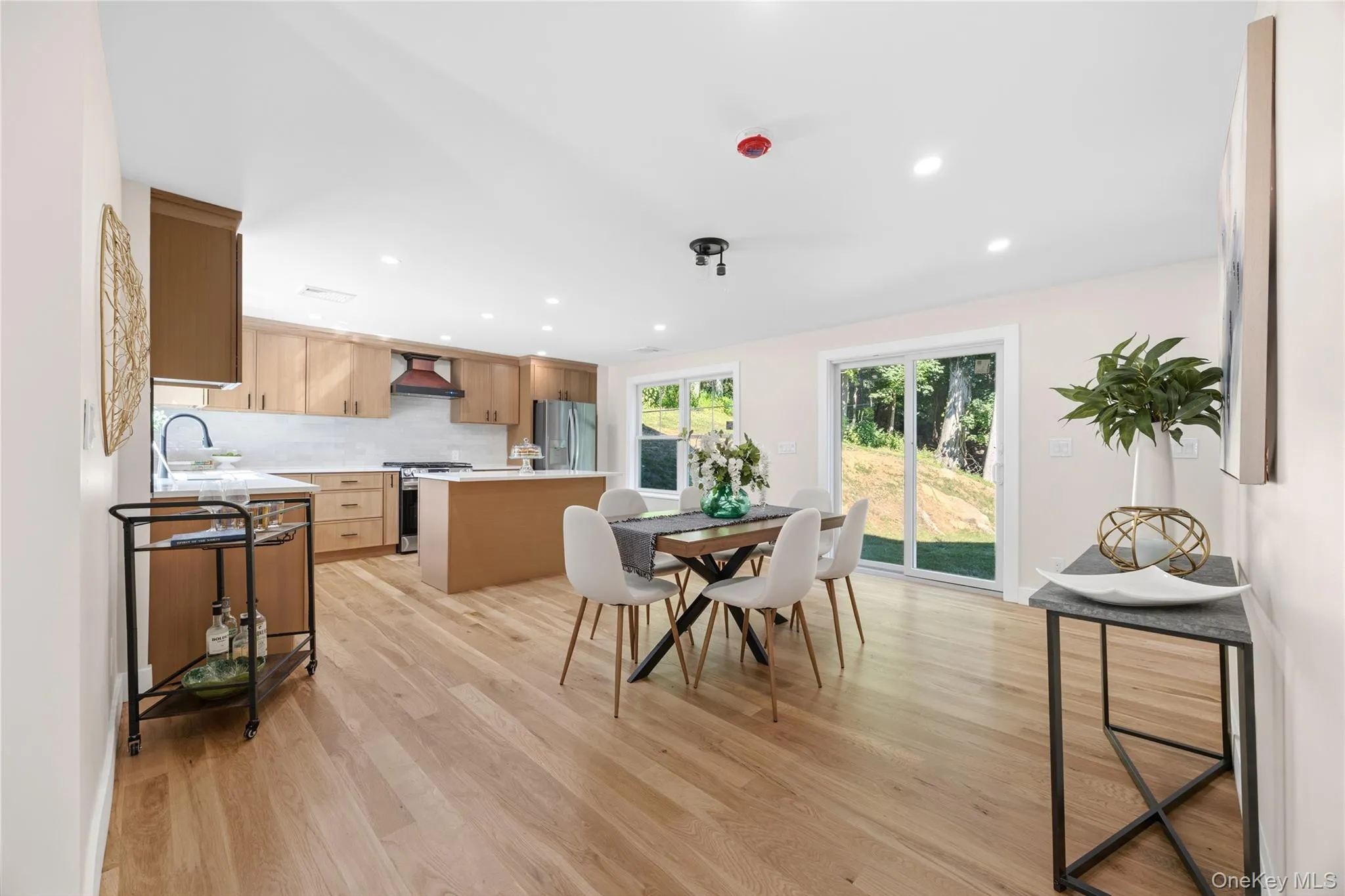 Open-concept living area with light wood-finish flooring, recessed lighting, and a kitchen featuring wood cabinetry Open-concept living area with light wood-finish flooring, recessed lighting, and a kitchen featuring wood cabinetry