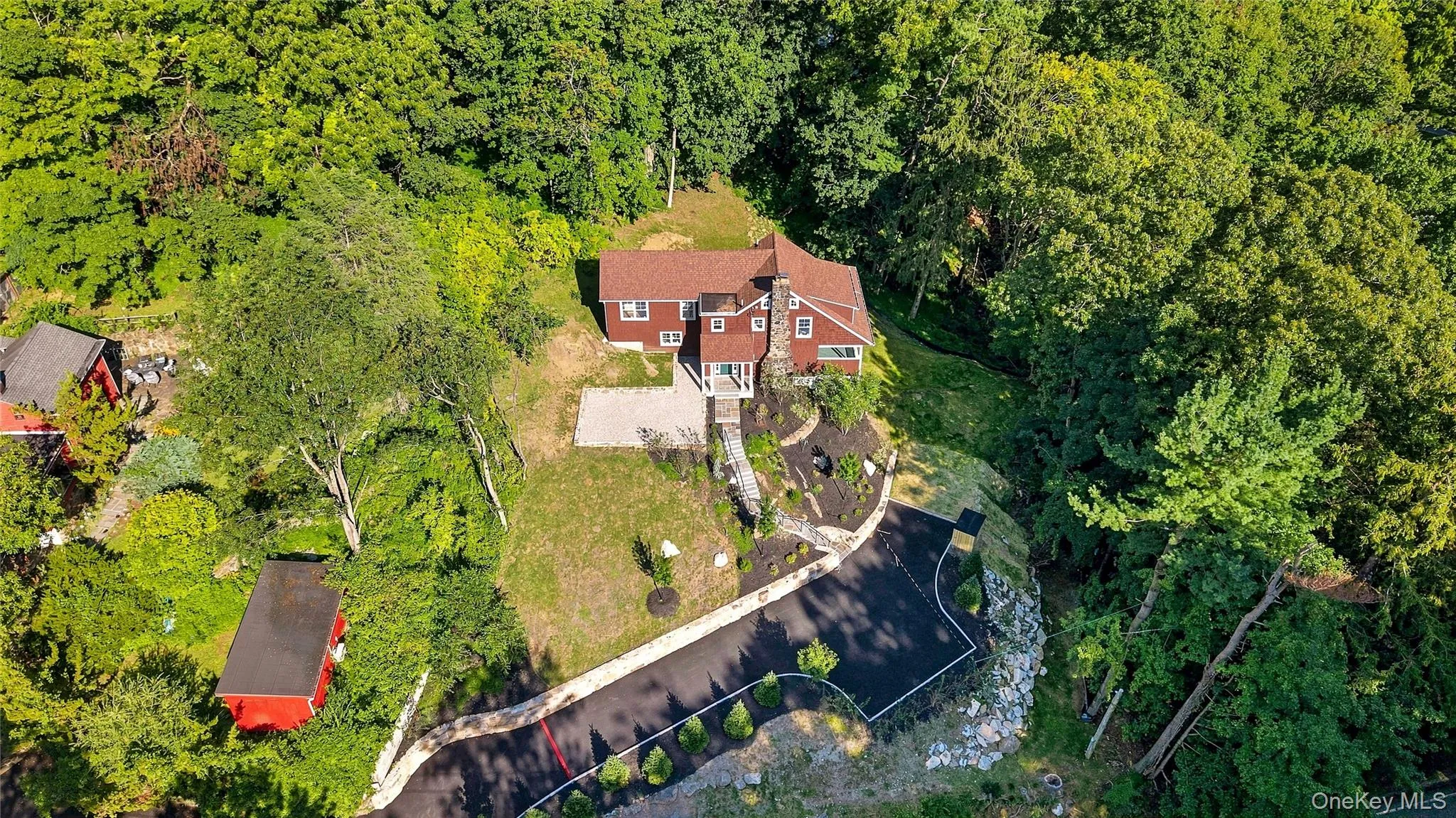Aerial perspective showcasing a red-sided residence with a brown shingle roof, a two-car asphalt driveway, and surrounding mature trees Aerial perspective showcasing a red-sided residence with a brown shingle roof, a two-car asphalt driveway, and surrounding mature trees
