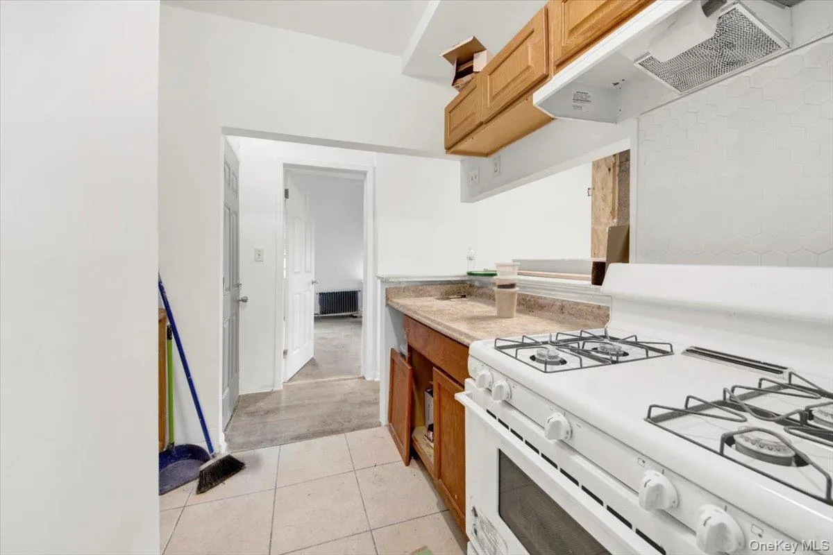 Kitchen featuring white gas range, wall chimney range hood, light countertops, and light tile patterned floors Kitchen featuring white gas range, wall chimney range hood, light countertops, and light tile patterned floors