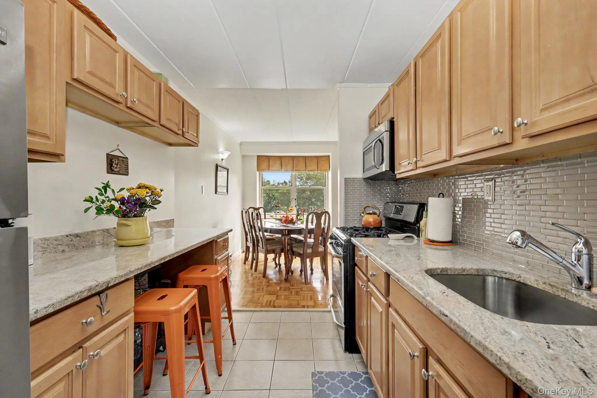 Galley kitchen featuring natural wood cabinetry, light stone countertops, stainless steel sink with chrome faucet, tile backsplash, and black appliances Galley kitchen featuring natural wood cabinetry, light stone countertops, stainless steel sink with chrome faucet, tile backsplash, and black appliances