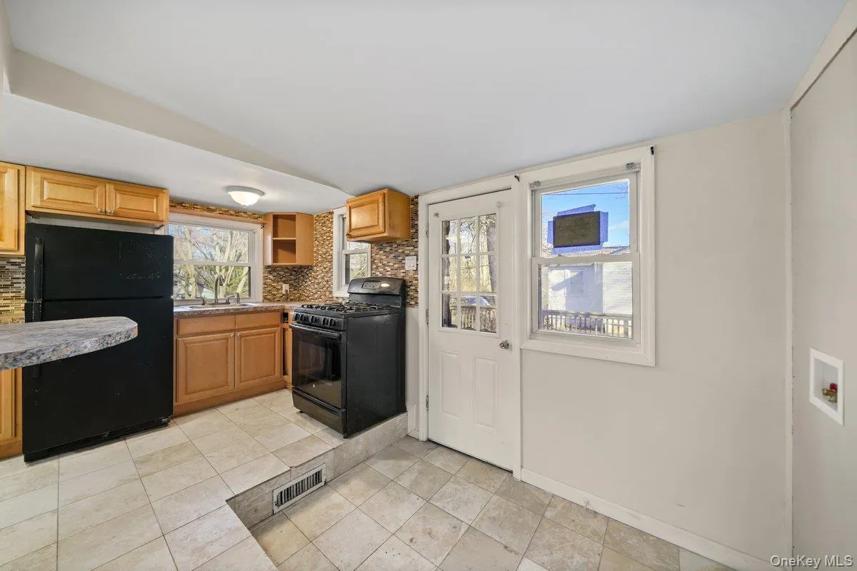 Kitchen with tasteful backsplash, black appliances, open shelves, light tile patterned flooring, and brown cabinets Kitchen with tasteful backsplash, black appliances, open shelves, light tile patterned flooring, and brown cabinets