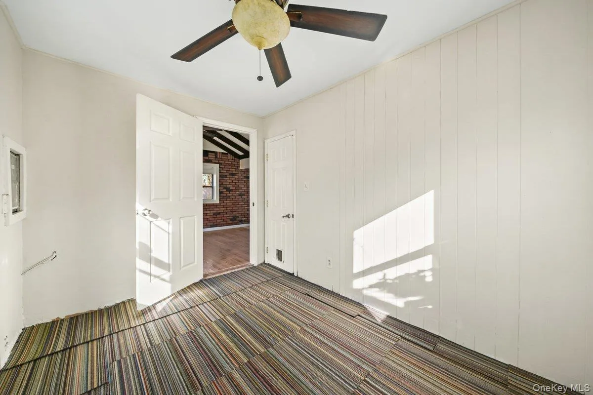 Unfurnished bedroom featuring dark colored carpet, brick wall, and ceiling fan Unfurnished bedroom featuring dark colored carpet, brick wall, and ceiling fan