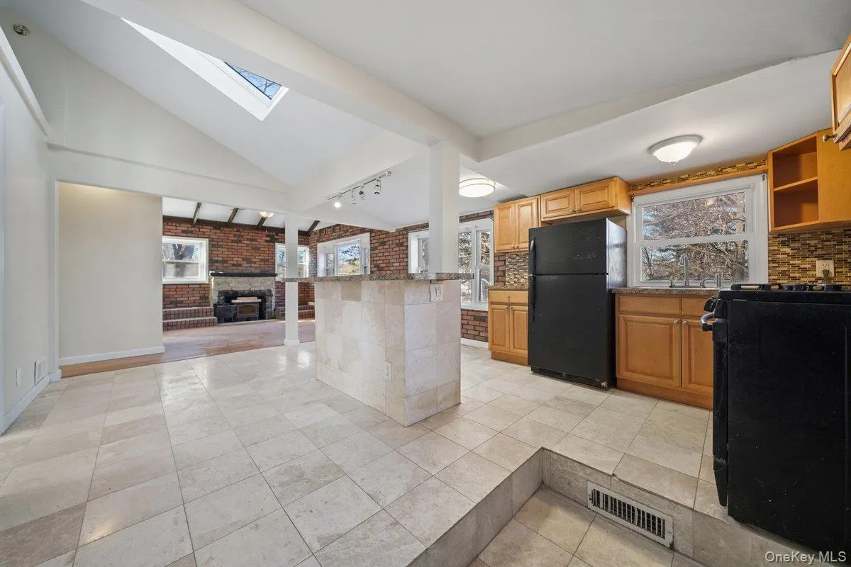 Kitchen with a brick fireplace, black appliances, open shelves, a skylight, and decorative backsplash Kitchen with a brick fireplace, black appliances, open shelves, a skylight, and decorative backsplash