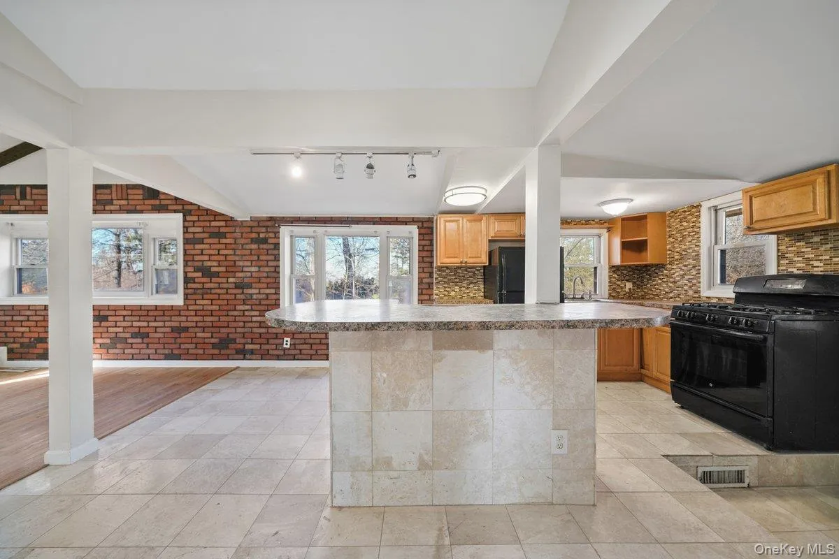 Kitchen featuring black appliances, backsplash, brick wall, a kitchen island, and light tile patterned floors Kitchen featuring black appliances, backsplash, brick wall, a kitchen island, and light tile patterned floors