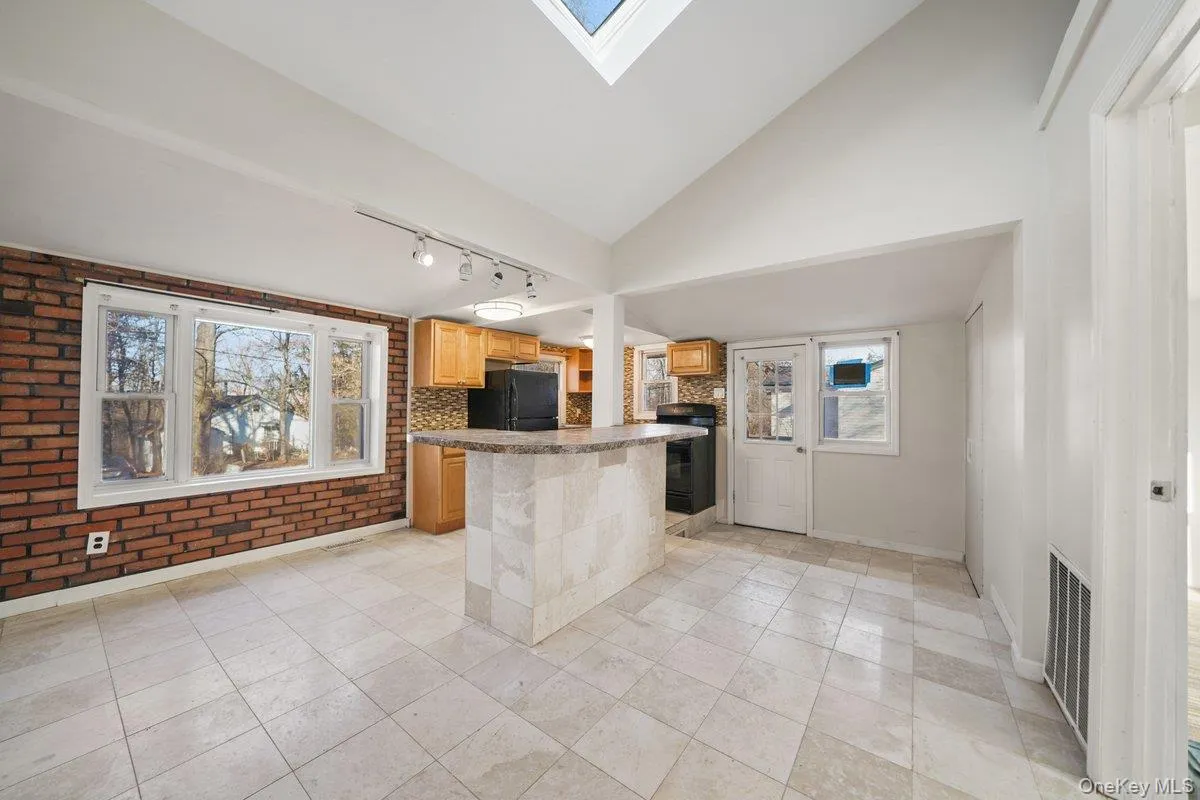 Kitchen featuring rail lighting, a skylight, brick wall, black appliances, and light tile patterned floors Kitchen featuring rail lighting, a skylight, brick wall, black appliances, and light tile patterned floors