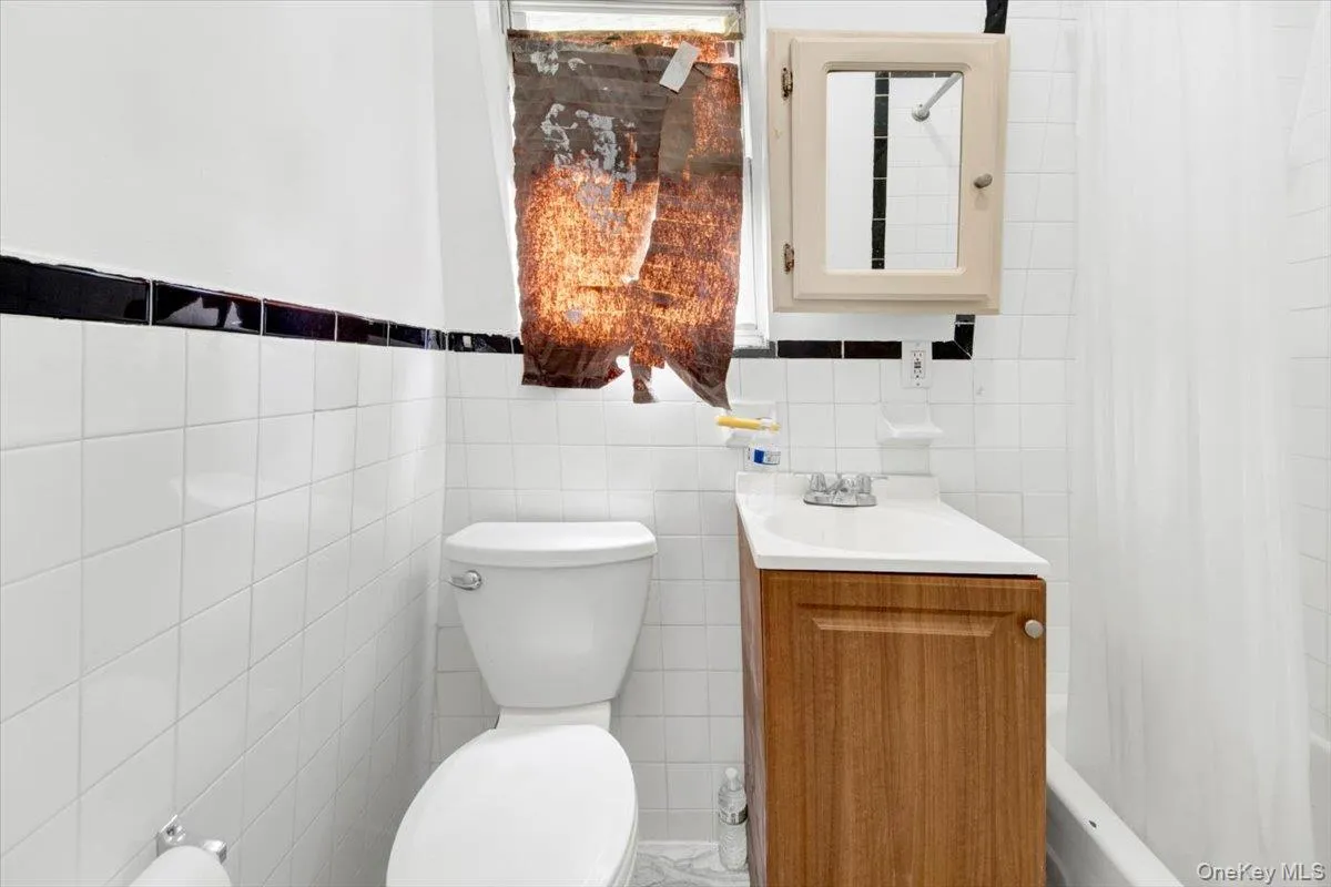 Bathroom with tile walls, toilet, vanity, and shower / tub combo with curtain Bathroom with tile walls, toilet, vanity, and shower / tub combo with curtain
