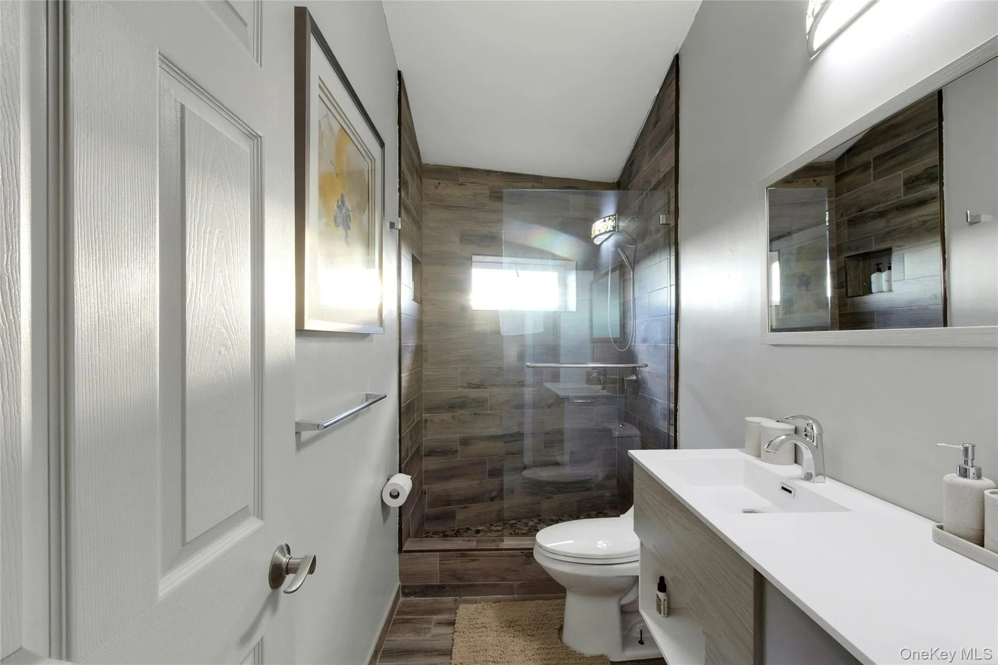 Bathroom featuring a walk-in shower with wood-finish tile surround, clear glass enclosure, and stone flooring Bathroom featuring a walk-in shower with wood-finish tile surround, clear glass enclosure, and stone flooring