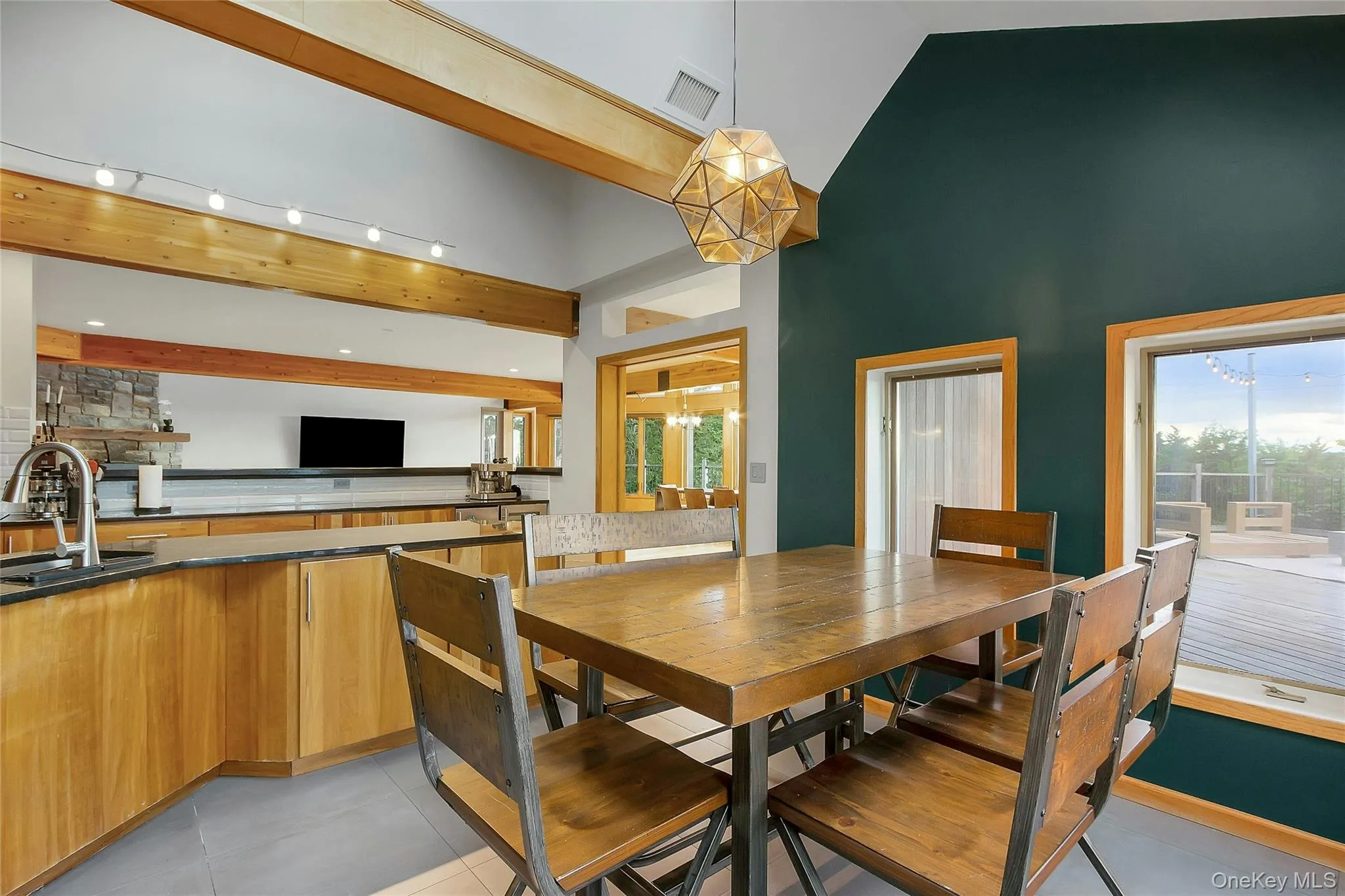 Vaulted ceiling, exposed wood beams, geometric pendant lighting, wood-finish cabinetry, and a built-in kitchen sink Vaulted ceiling, exposed wood beams, geometric pendant lighting, wood-finish cabinetry, and a built-in kitchen sink