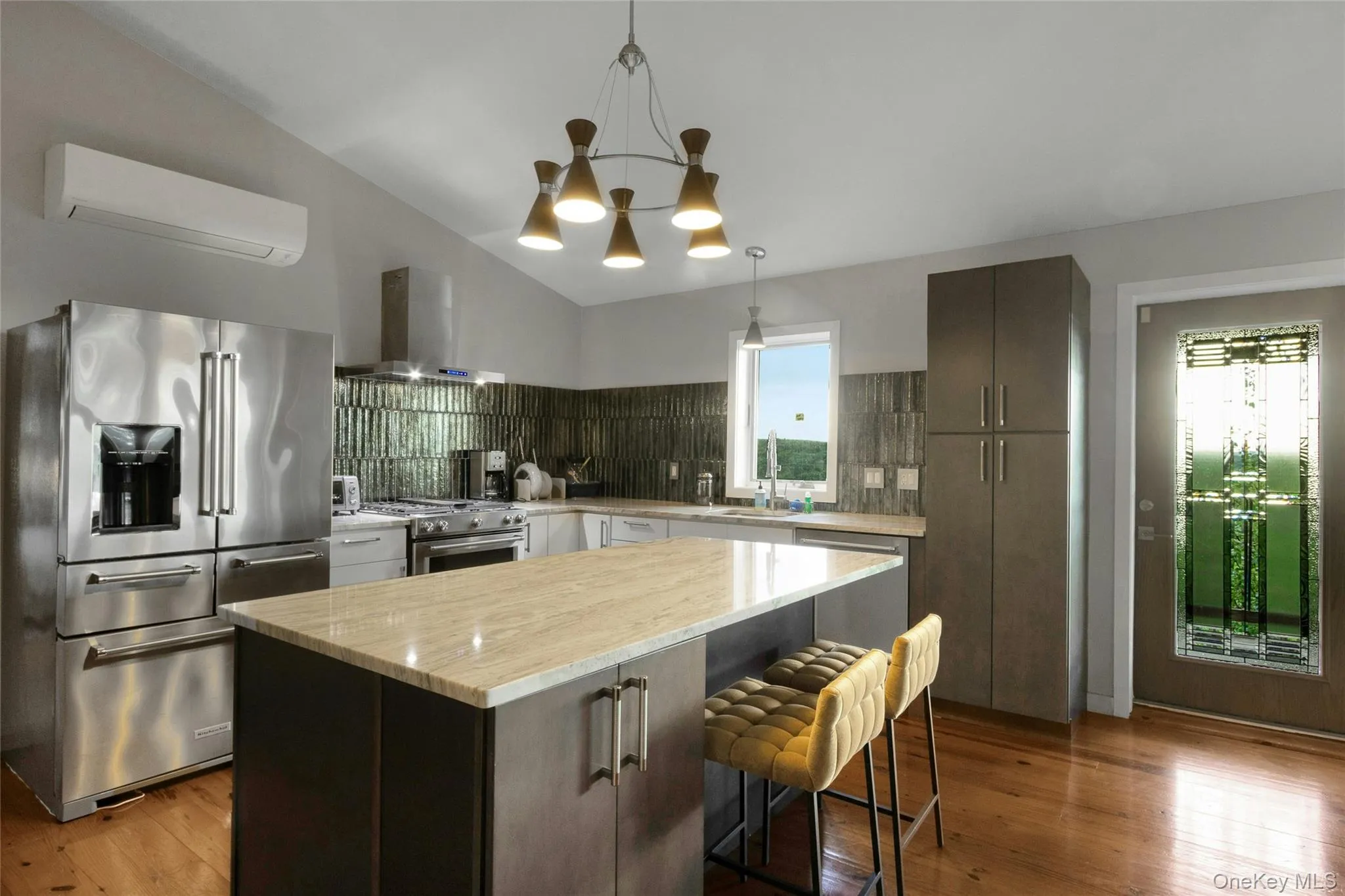 Kitchen featuring a vaulted ceiling, wood-finish flooring, stainless steel appliances, a center island with countertop, and a decorative glass door Kitchen featuring a vaulted ceiling, wood-finish flooring, stainless steel appliances, a center island with countertop, and a decorative glass door