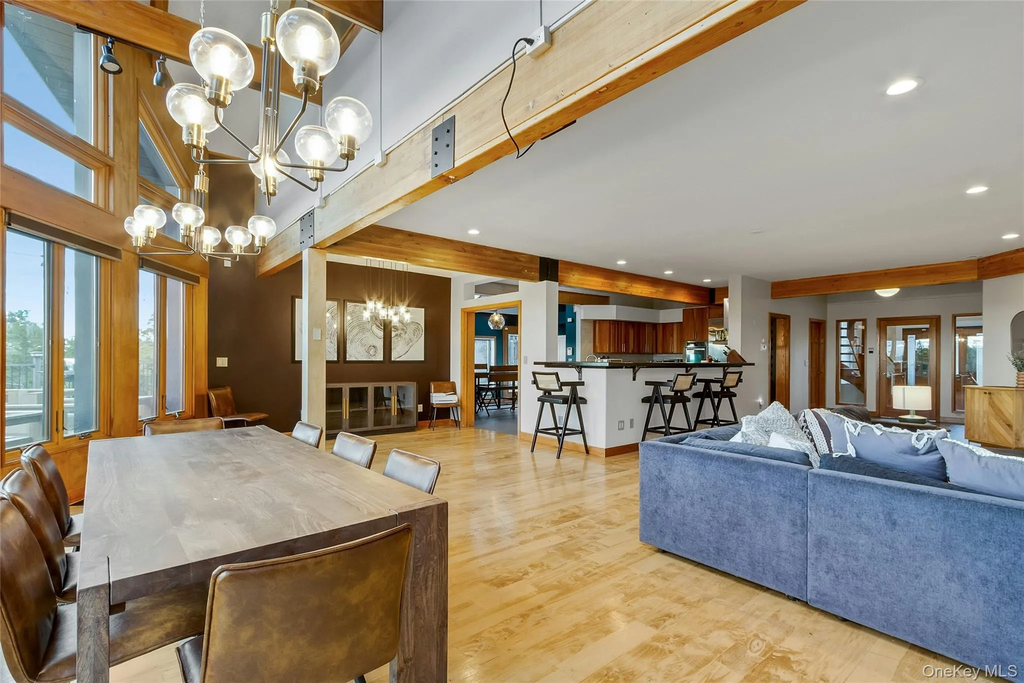 Expansive living area with wood-finish flooring, exposed wood beams, and large windows Expansive living area with wood-finish flooring, exposed wood beams, and large windows