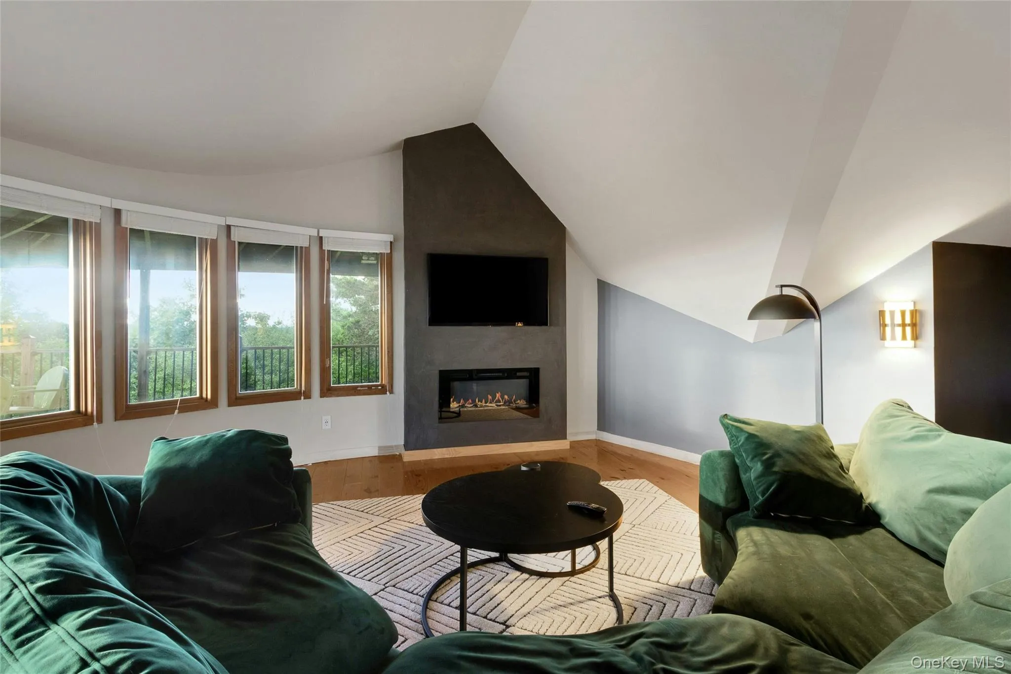 Recessed electric fireplace set in a dark-toned accent wall, light wood-finish flooring, and multiple large windows with natural wood frames Recessed electric fireplace set in a dark-toned accent wall, light wood-finish flooring, and multiple large windows with natural wood frames