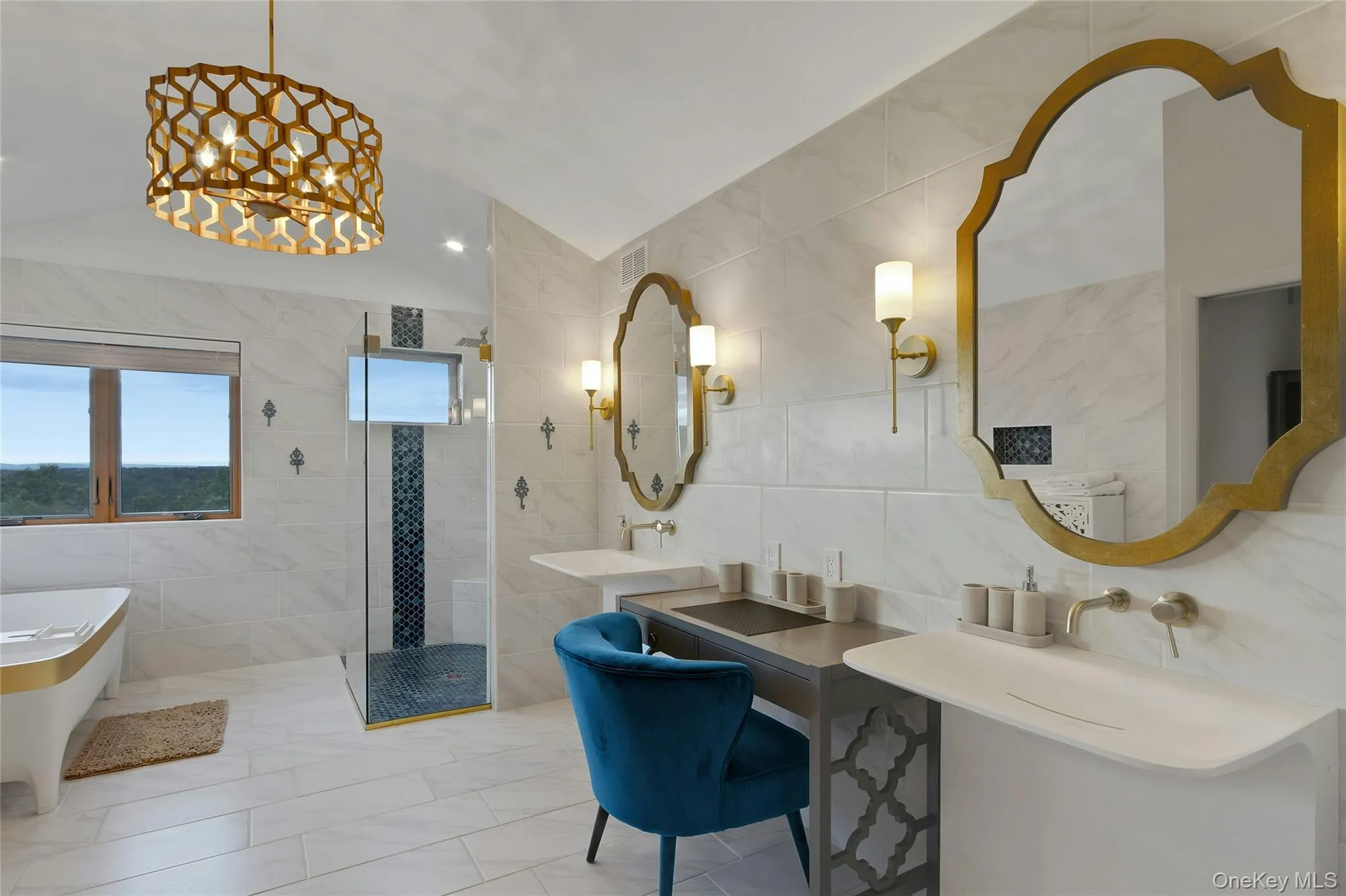 Freestanding soaking tub with gold accent, glass-enclosed shower with tiled accent wall, dual wall-mounted sinks, and ornate gold-framed mirrors Freestanding soaking tub with gold accent, glass-enclosed shower with tiled accent wall, dual wall-mounted sinks, and ornate gold-framed mirrors