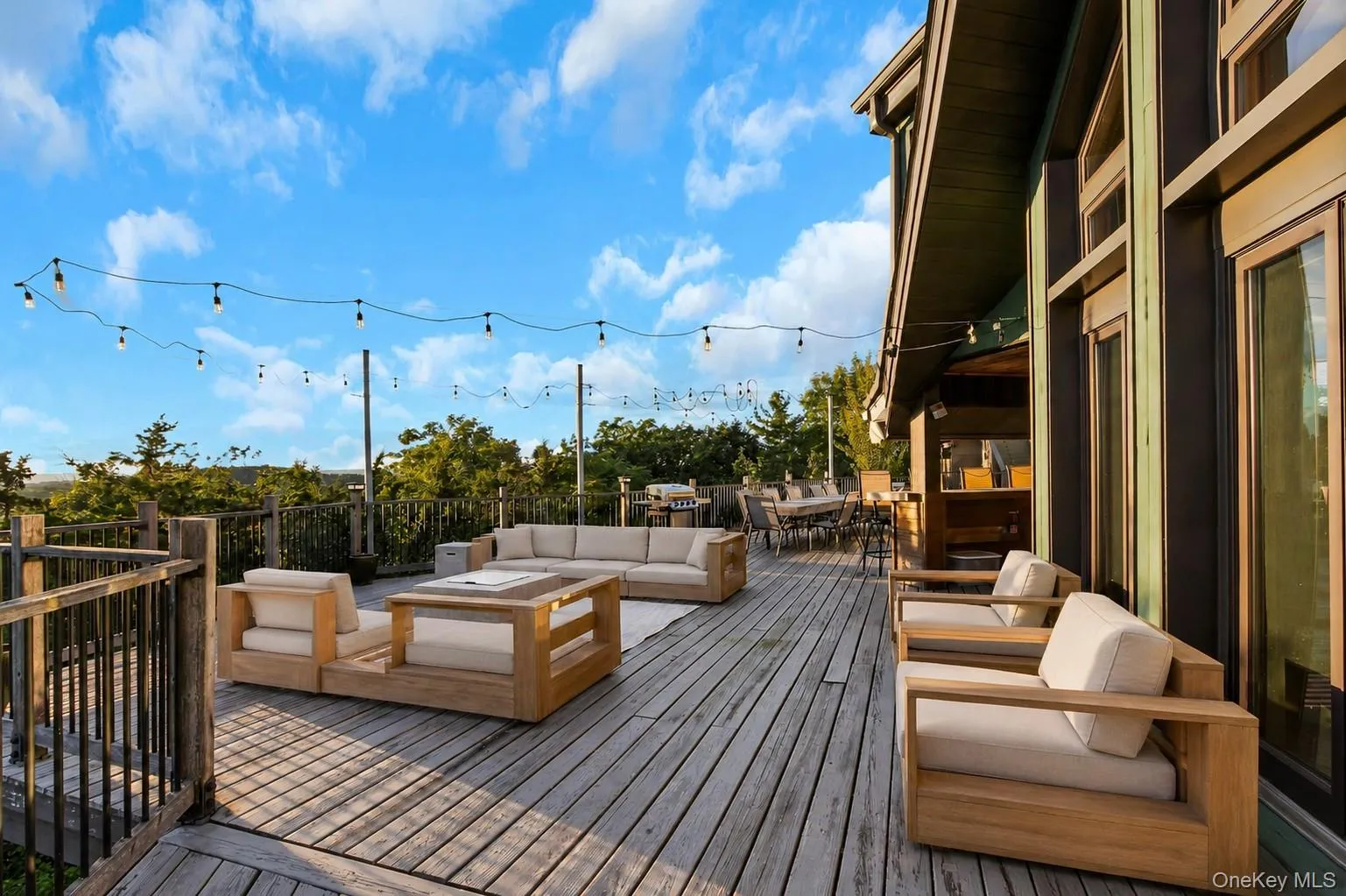 Expansive wood deck with string lighting, multiple seating areas, and a built-in outdoor kitchen Expansive wood deck with string lighting, multiple seating areas, and a built-in outdoor kitchen