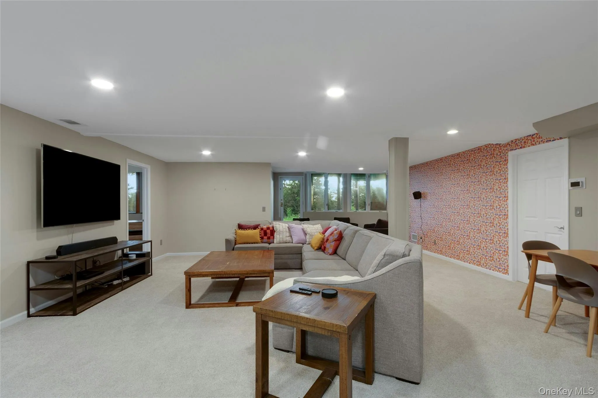 Recessed lighting illuminating a spacious carpeted area, featuring an accent wall and a built-in entertainment stand Recessed lighting illuminating a spacious carpeted area, featuring an accent wall and a built-in entertainment stand
