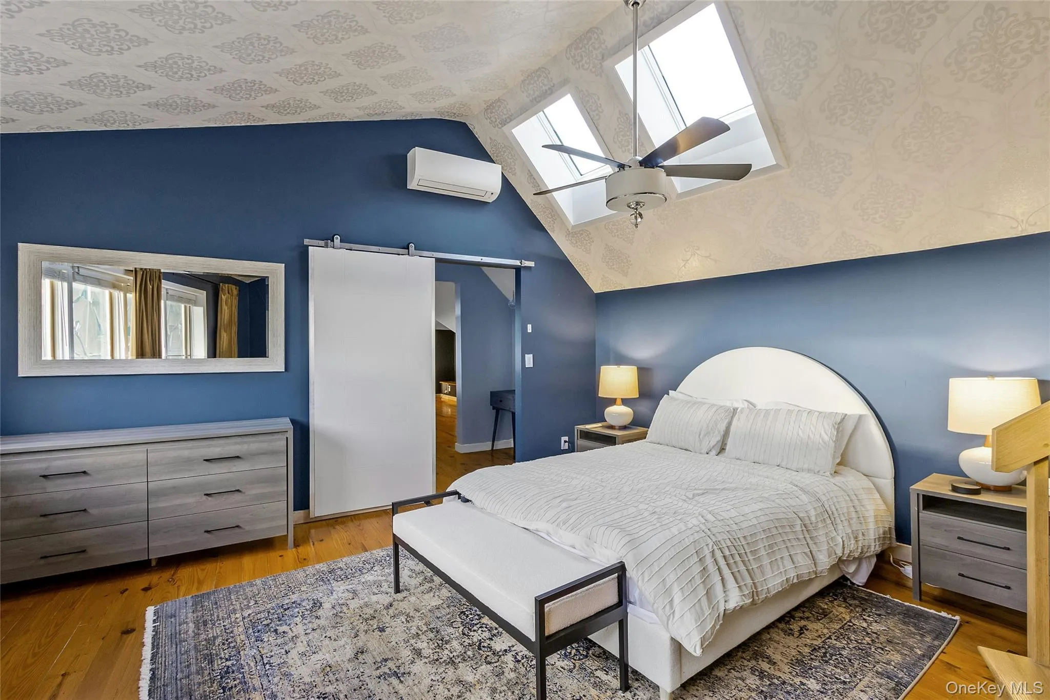 Hardwood flooring, sloped ceiling with patterned accent, skylights, ceiling fan, and barn door entry Hardwood flooring, sloped ceiling with patterned accent, skylights, ceiling fan, and barn door entry