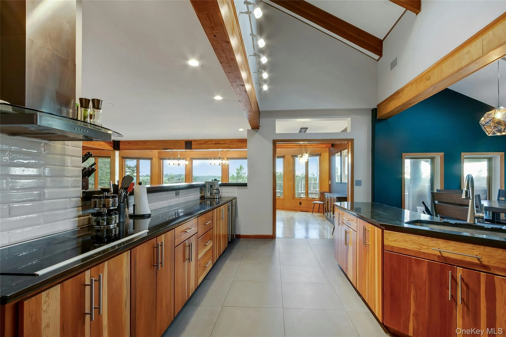 Vaulted ceilings with exposed wood beams, wood-finish cabinetry, dark countertops, a stainless steel range hood, and tile flooring Vaulted ceilings with exposed wood beams, wood-finish cabinetry, dark countertops, a stainless steel range hood, and tile flooring