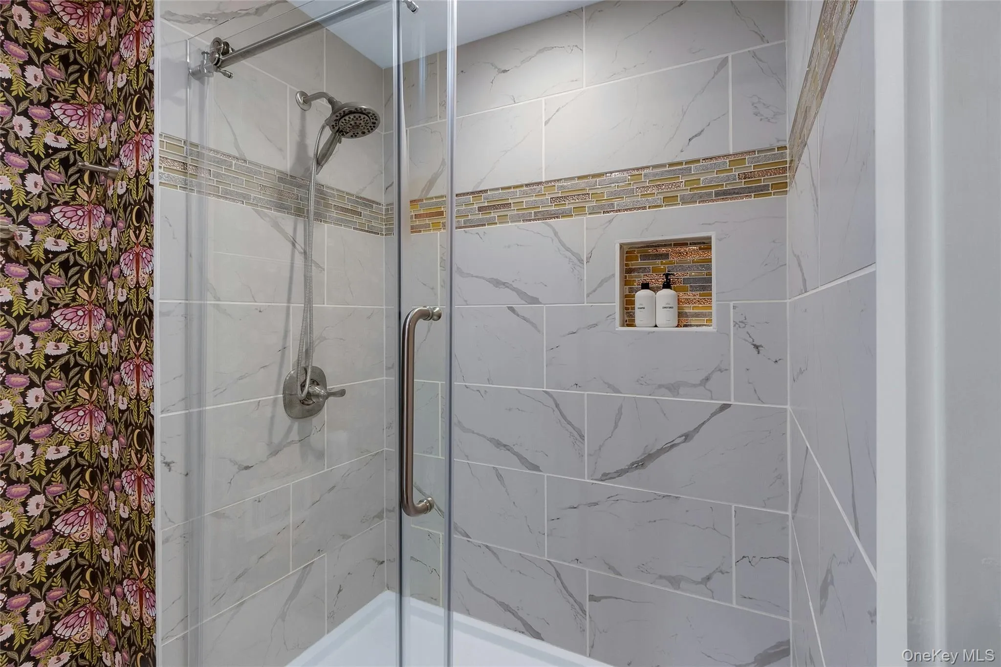 Glass-enclosed shower featuring large format tile with mosaic accent, built-in recessed shelf, and a brushed nickel shower fixture Glass-enclosed shower featuring large format tile with mosaic accent, built-in recessed shelf, and a brushed nickel shower fixture