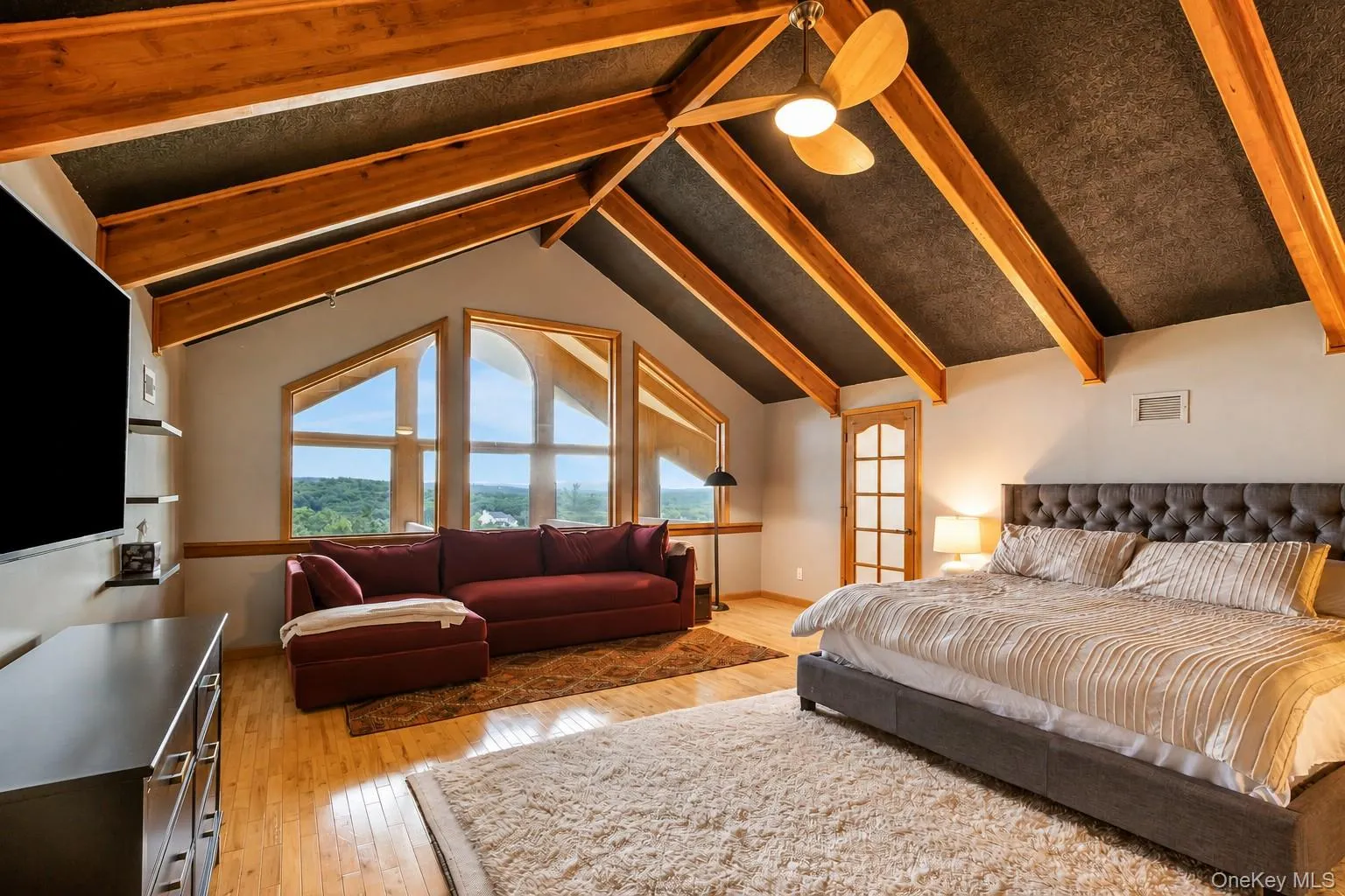 Vaulted ceiling with exposed wood beams, hardwood flooring, large transom windows, and a ceiling fan with light fixture Vaulted ceiling with exposed wood beams, hardwood flooring, large transom windows, and a ceiling fan with light fixture