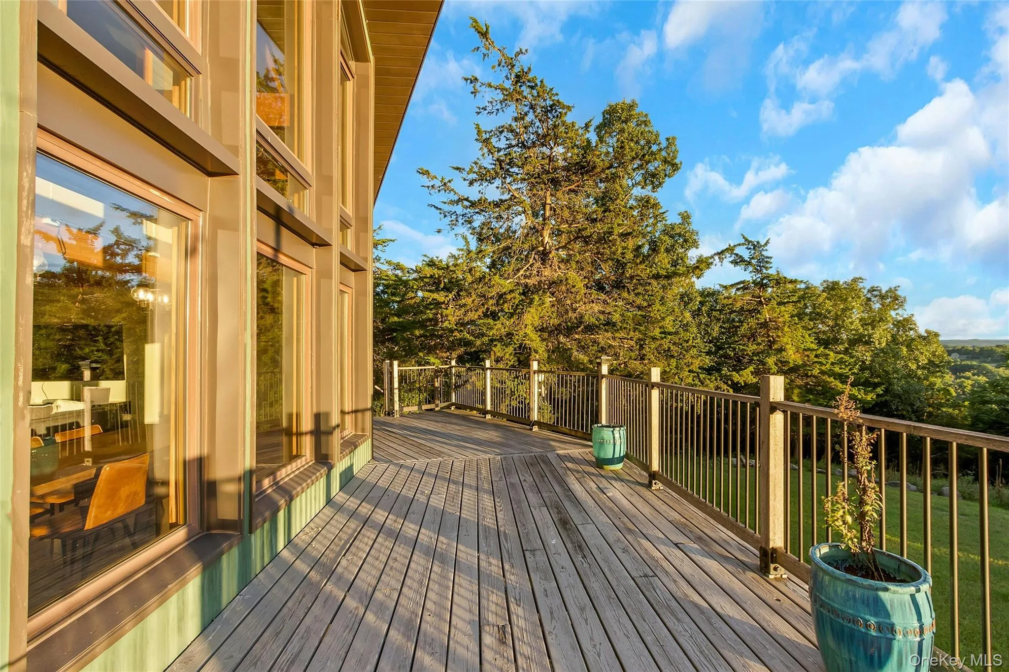 Expansive outdoor deck with wood plank flooring and metal railings, complemented by large vertical windows with wood frames Expansive outdoor deck with wood plank flooring and metal railings, complemented by large vertical windows with wood frames