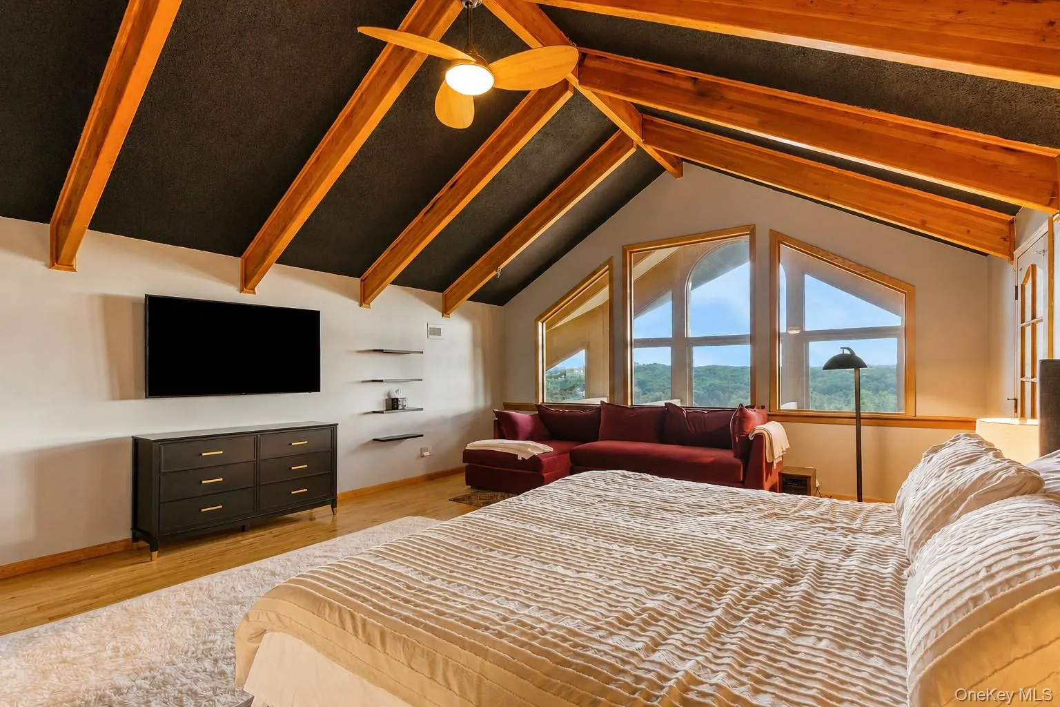 Vaulted ceiling with exposed wood beams, ceiling fan, hardwood flooring, built-in shelving, and large picture windows Vaulted ceiling with exposed wood beams, ceiling fan, hardwood flooring, built-in shelving, and large picture windows