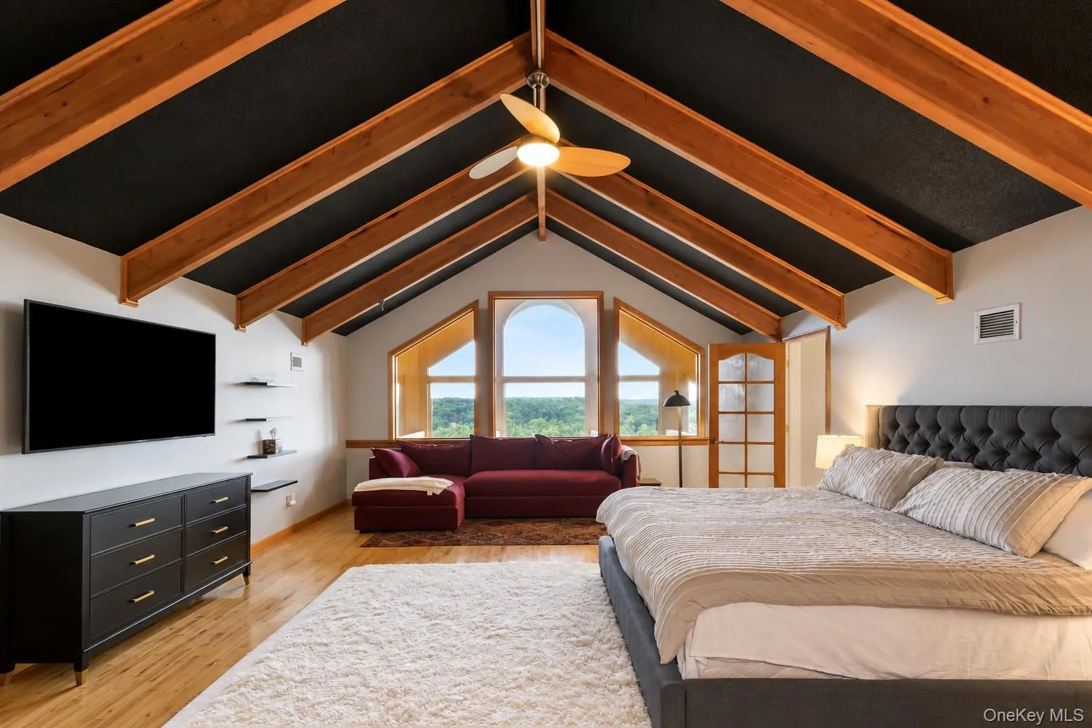 Vaulted ceiling with exposed wood beams, arched windows, light wood-finish flooring, and a ceiling fan Vaulted ceiling with exposed wood beams, arched windows, light wood-finish flooring, and a ceiling fan