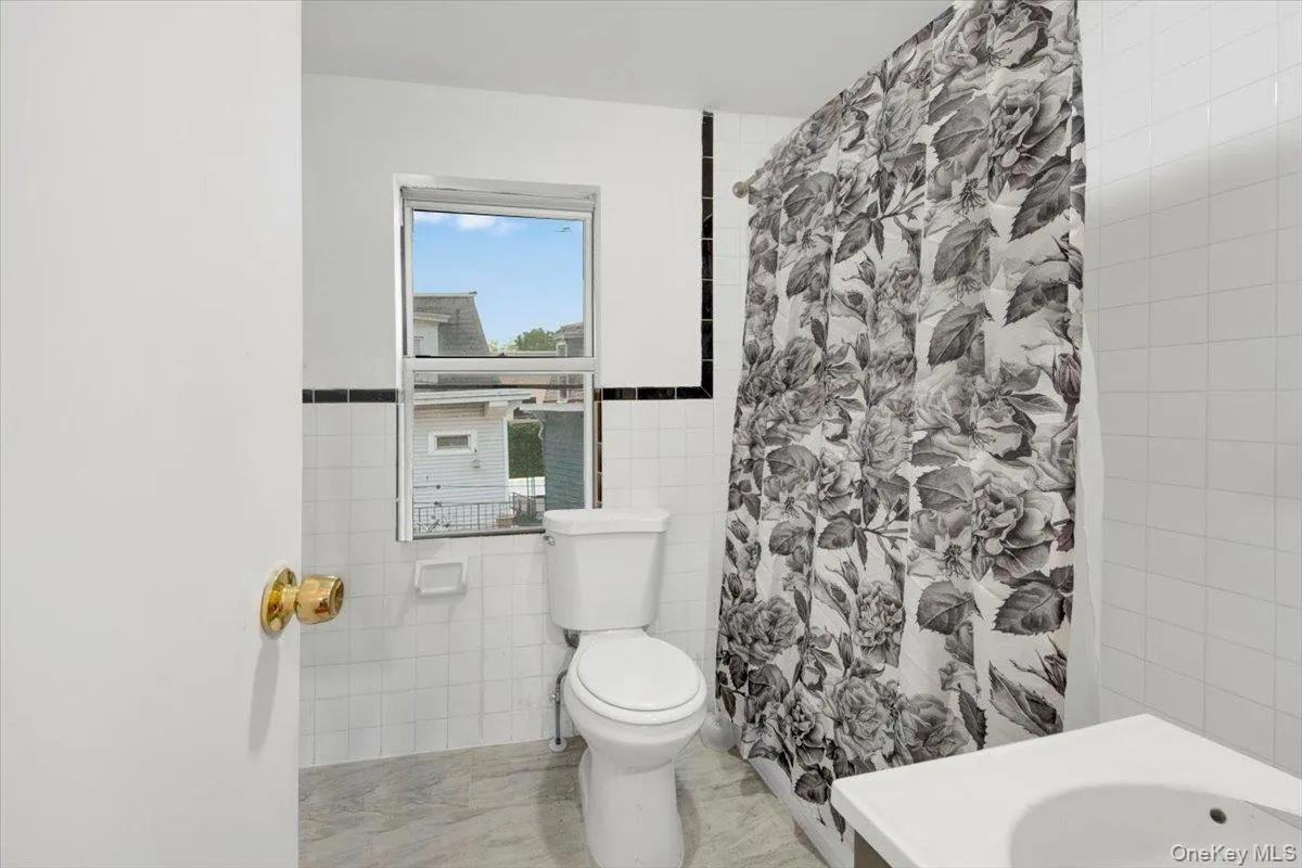 Full bathroom with tile walls, toilet, a shower with curtain, vanity, and marble finish floors Full bathroom with tile walls, toilet, a shower with curtain, vanity, and marble finish floors