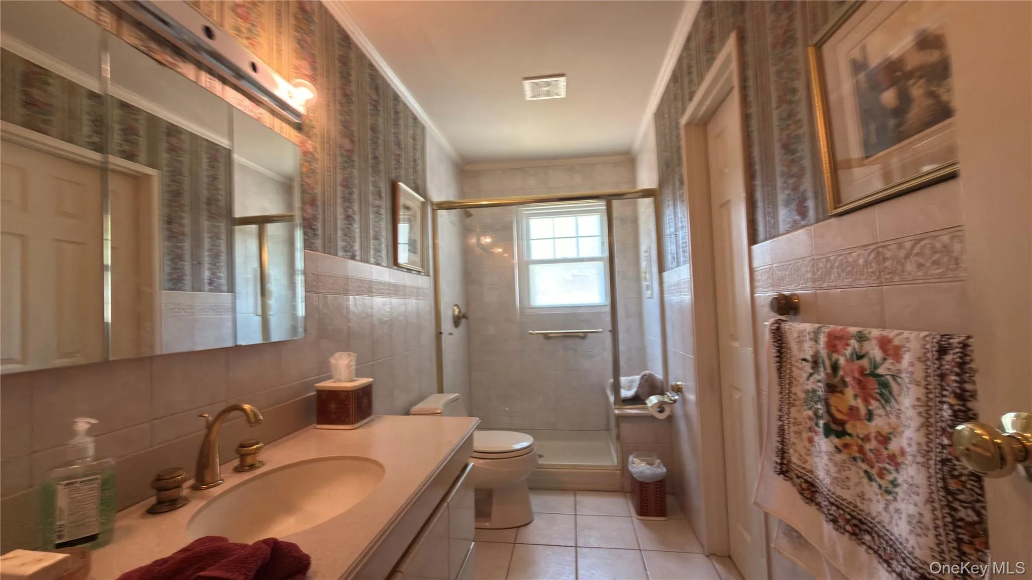 Vanity with integrated sink, brass fixtures, mirrored medicine cabinet, tiled shower with glass enclosure, and a window Vanity with integrated sink, brass fixtures, mirrored medicine cabinet, tiled shower with glass enclosure, and a window