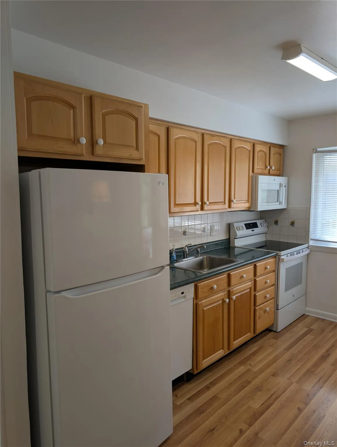 Kitchen with wood-finish flooring, maple wood cabinetry, newer white appliances, and a dark countertop Kitchen with wood-finish flooring, maple wood cabinetry, newer white appliances, and a dark countertop