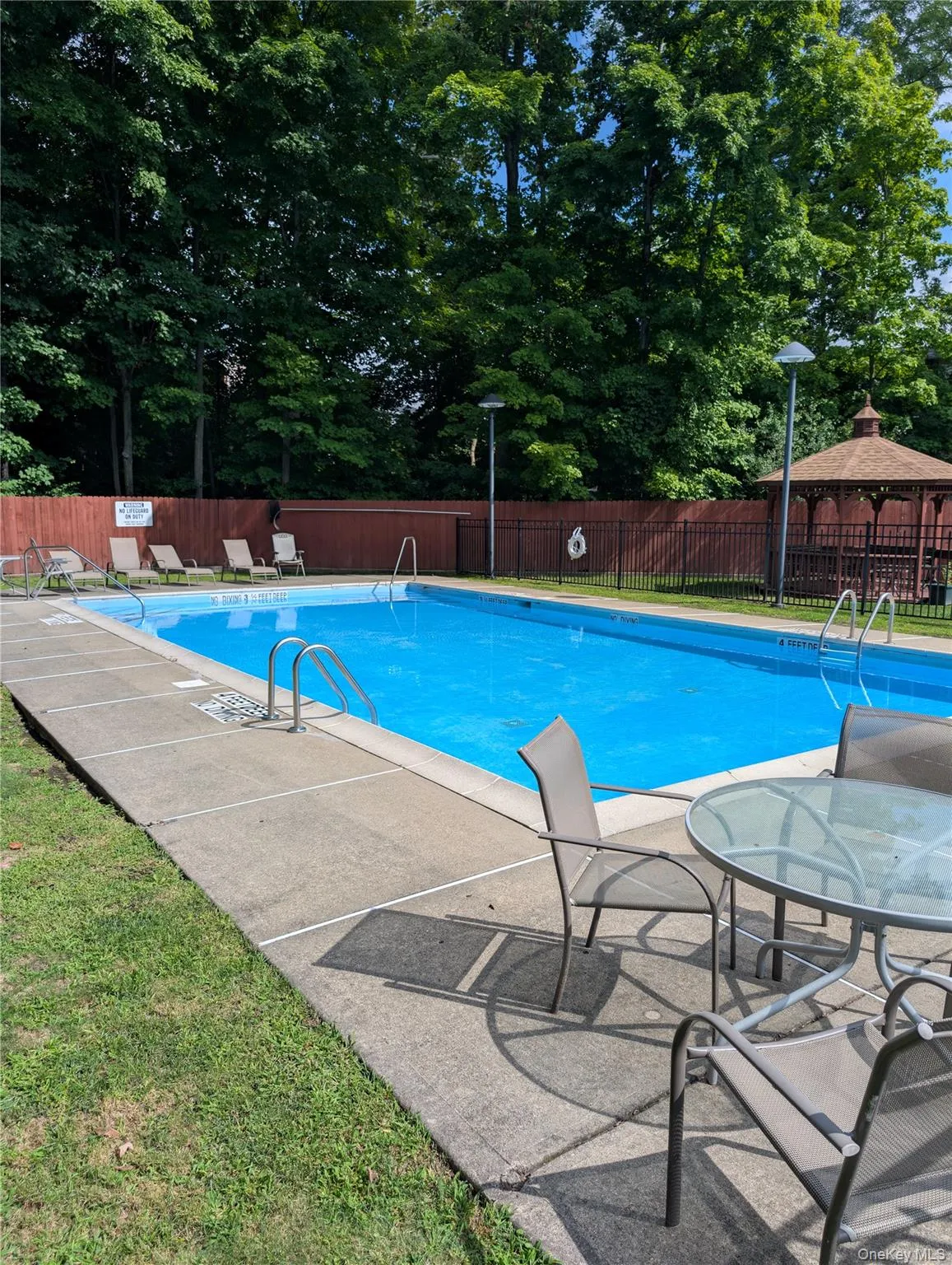 Fenced outdoor swimming pool with concrete surround and furniture Fenced outdoor swimming pool with concrete surround and furniture