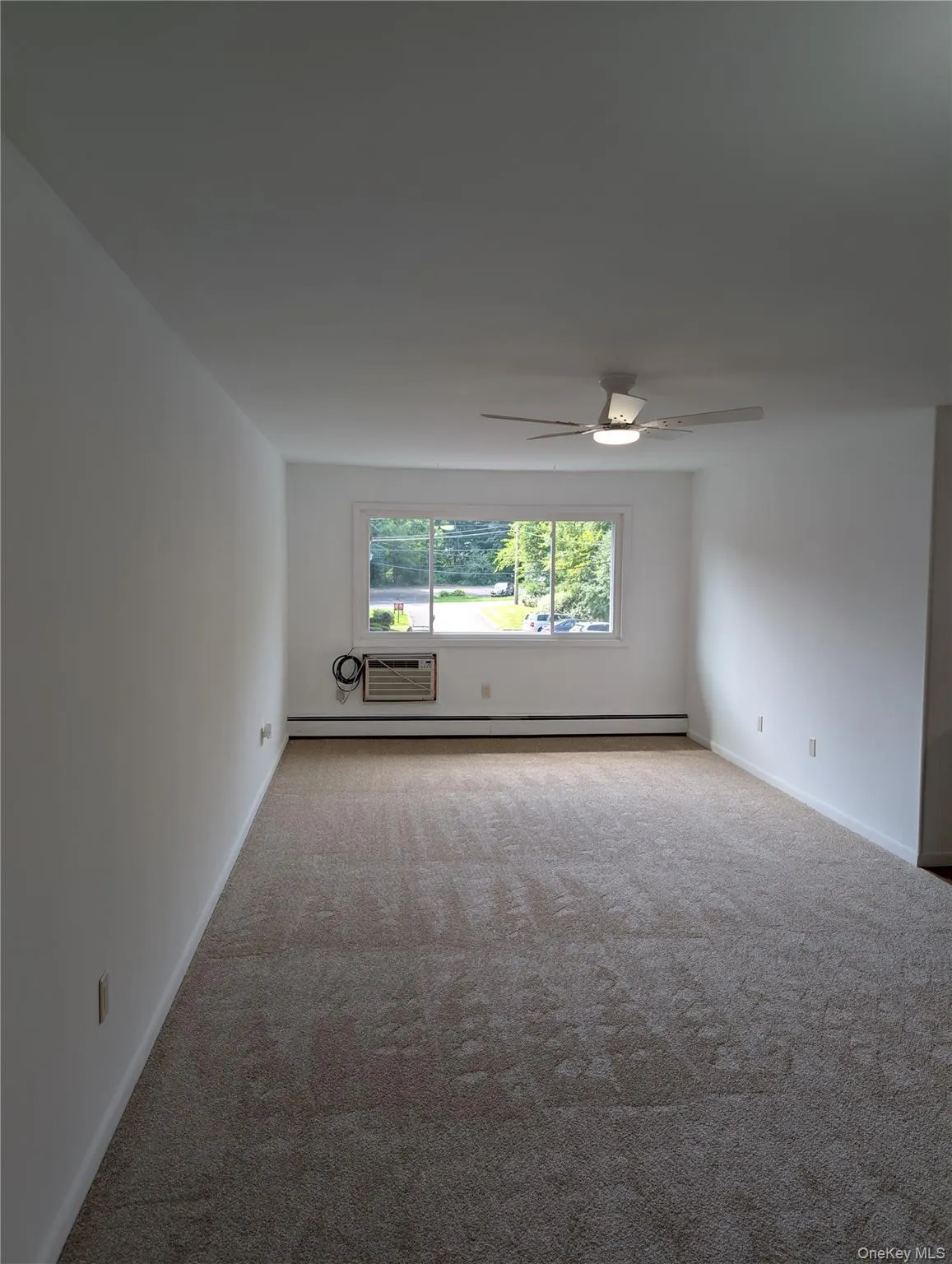 Neutral-toned carpeting, white walls, and an in-wall air conditioning unit ceiling fan/light unit Neutral-toned carpeting, white walls, and an in-wall air conditioning unit ceiling fan/light unit