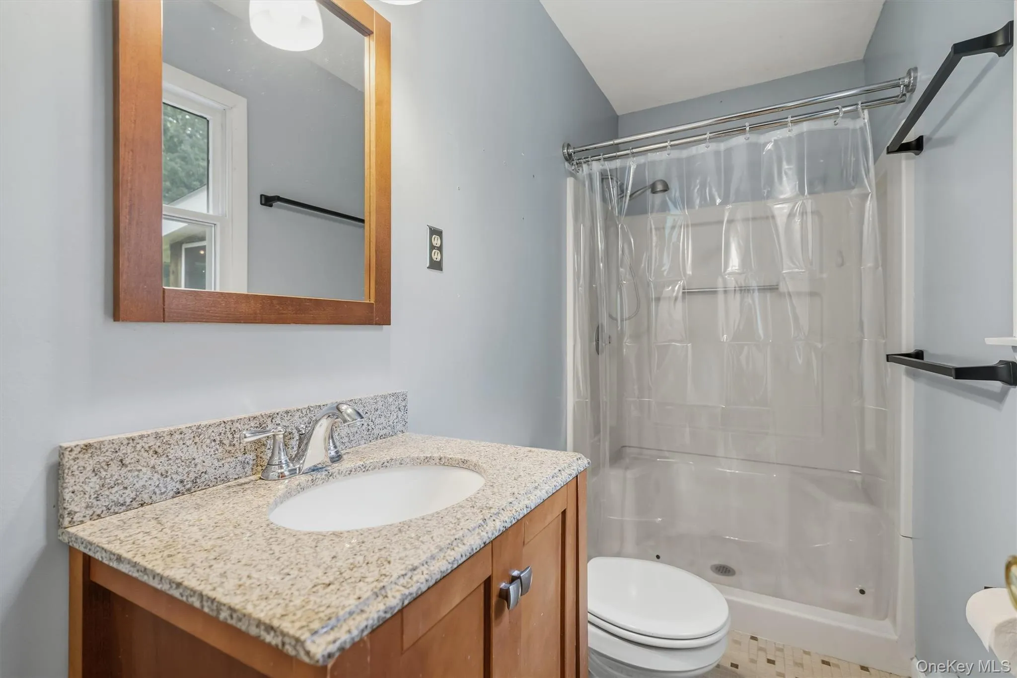 Bathroom featuring a wood-finish vanity, light-toned stone countertop, integrated sink, and a shower Bathroom featuring a wood-finish vanity, light-toned stone countertop, integrated sink, and a shower