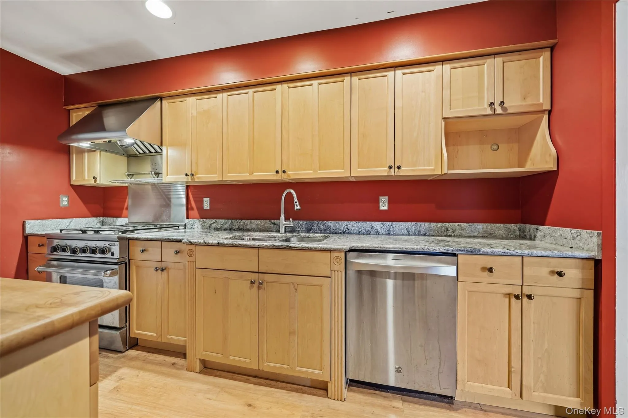 Wood-finish flooring with light-toned cabinetry, stainless steel appliances, a stainless steel range hood, and granite countertops Wood-finish flooring with light-toned cabinetry, stainless steel appliances, a stainless steel range hood, and granite countertops
