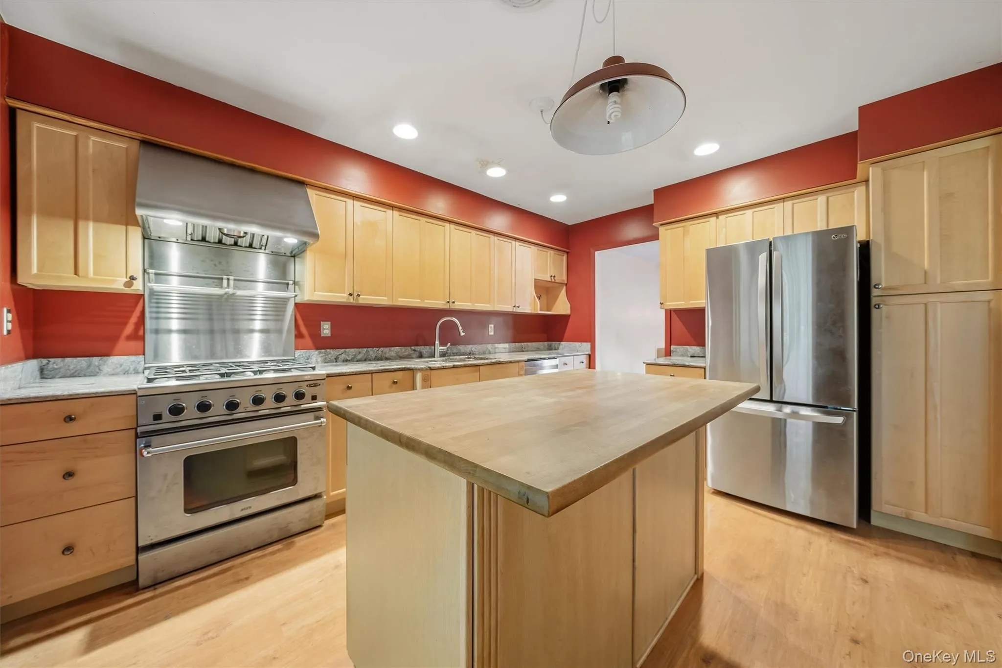 Kitchen featuring stainless steel appliances, wood-finish flooring, light wood cabinetry, a center island with a wood countertop, and recessed lighting Kitchen featuring stainless steel appliances, wood-finish flooring, light wood cabinetry, a center island with a wood countertop, and recessed lighting
